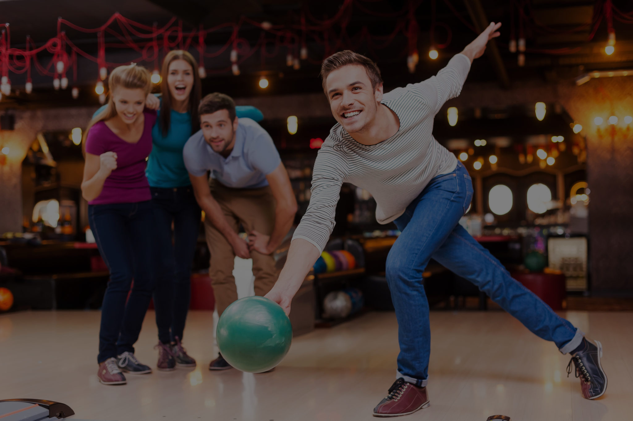 He is a winner. Handsome young men throwing a bowling ball while three people cheering